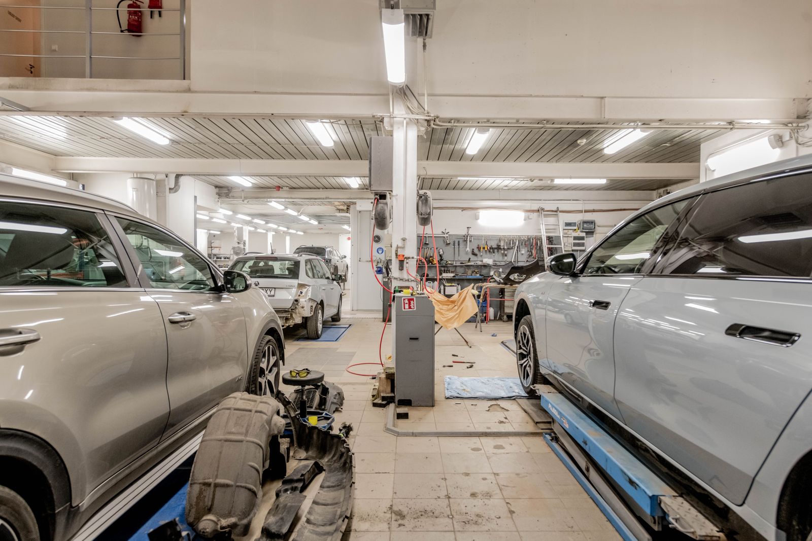 The inside of a busy repair workshop, cars raised on lifts and removed parts on the floor